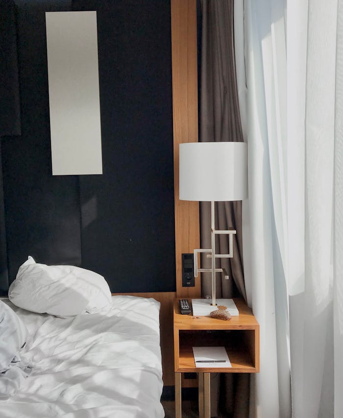 A contemporary bedroom with natural light featuring a bed, nightstand, and lamp.